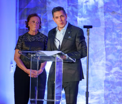 Picture of man wearing suit speaking at podium with woman in dress standing behind