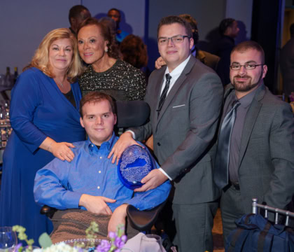 Man in blue button up shirt sitting and facing camera with four other people holding award