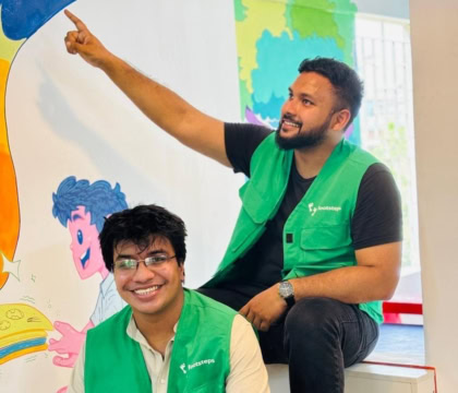 Photo of two men wearing green vests looking at camera, one man is smiling and another is pointing upwards