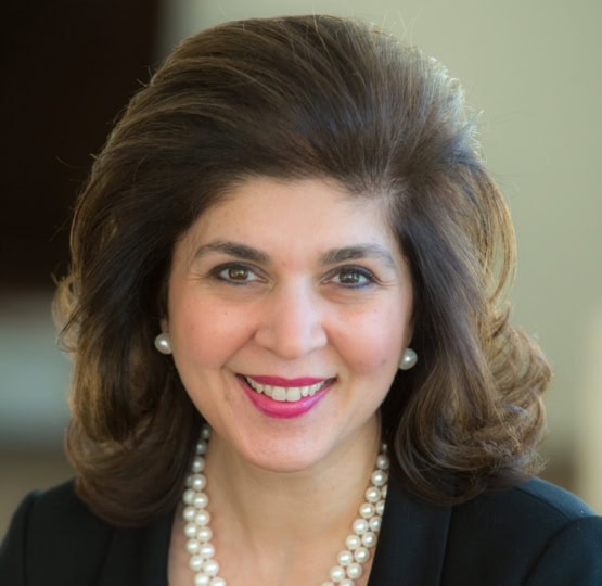 Photo of woman with dark hair wearing black top and white beaded necklace smiling at camera