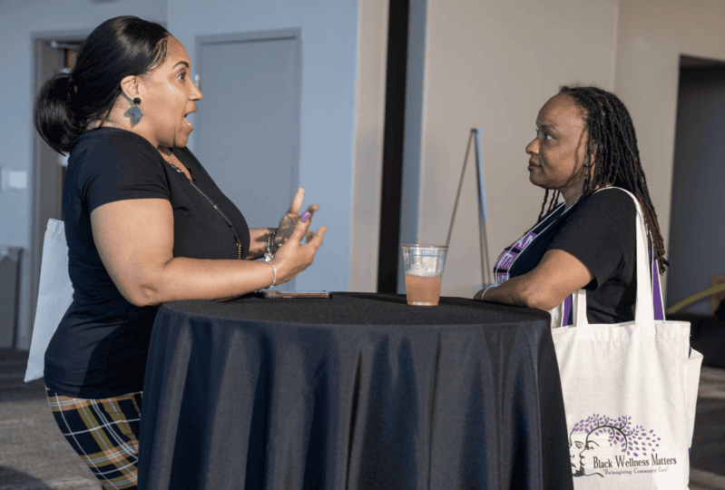 Two women standing at long table looking at each other and talking