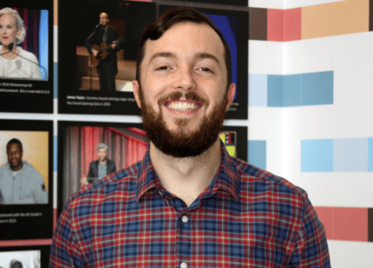 Picture of man with short hair and beard wearing red and blue button-up shirt smiling at camera