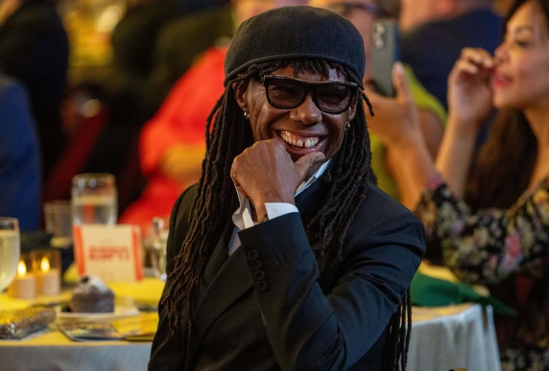 Photo of Nile Rodgers sitting at table and smiling to someone off camera