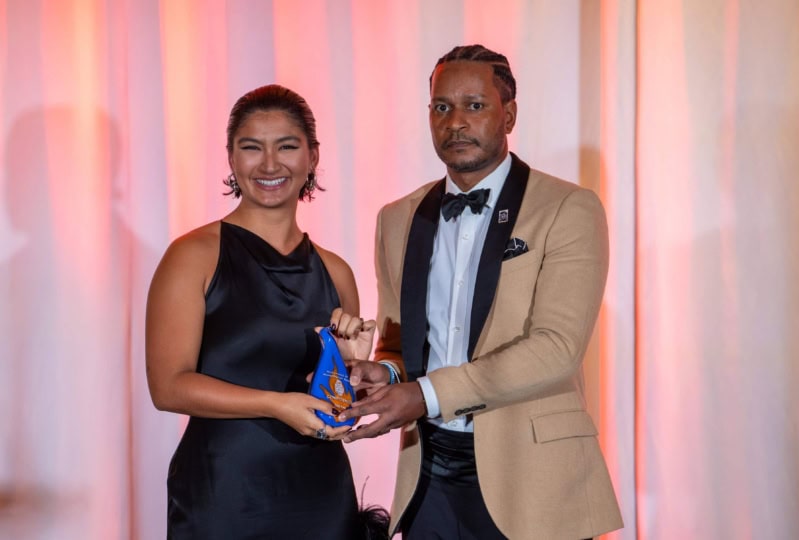 Photo of man in brown jacket and woman in black dress posing and holding award