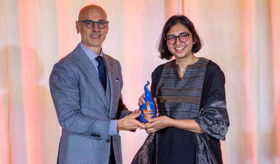 Photo of man in gray suit with glasses posing with woman with short dark hair and black top holding a Humanitarian Award shaped like a flame