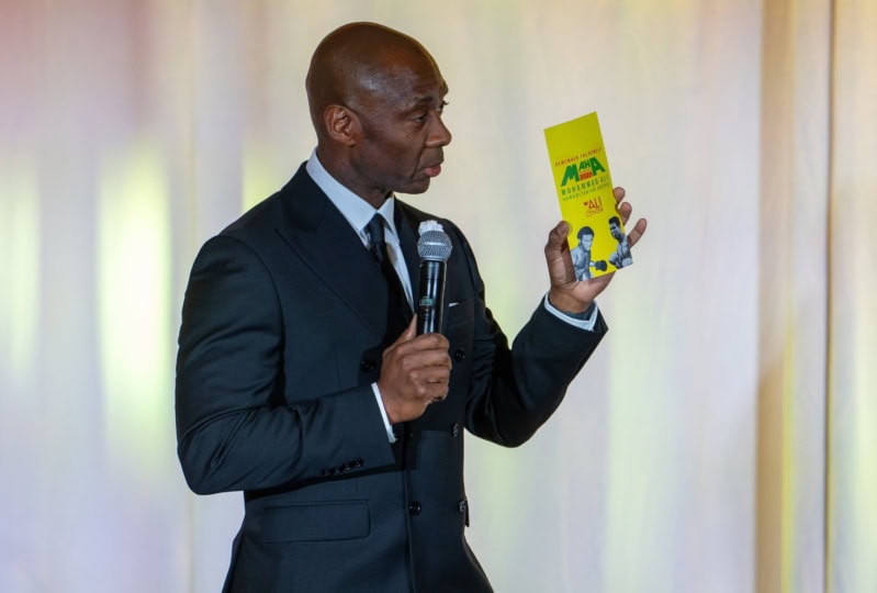 Photo of DeVone Holt in black suit holding Muhammad Ali Humanitarian Award program