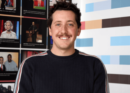 Picture of man with short curly hair and dark sweater smiling at camera