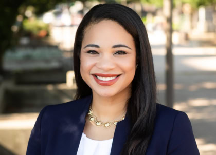 Photo of woman with dark hair wearing navy blue blazer smiling at camera