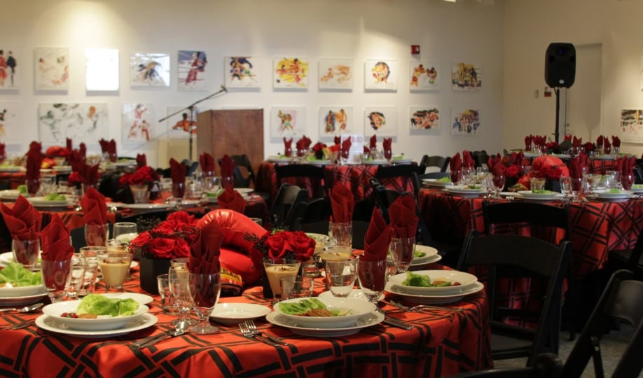 Art gallery set up for an event with large banquet rounds, red tablecloths, and black folding chairs