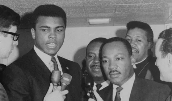 Black and white photo of Muhammad Ali and Martin Luther King Jr. in suits being interviewed