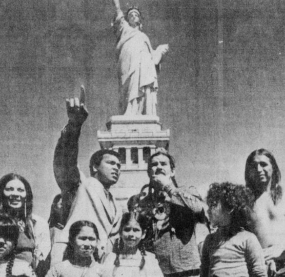 Photo of newspaper clipping with picture of Muhammad Ali standing with group of people near Statue of Liberty