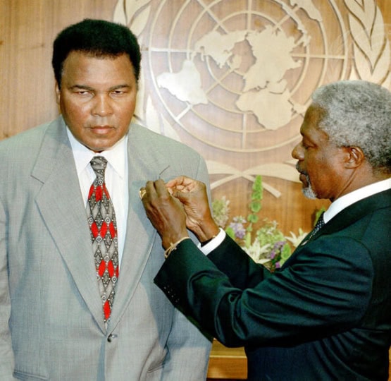 Photo of Muhammad Ali in gray suit receiving UN Messenger of Peace pin from UN Secretary General Kofi Annan