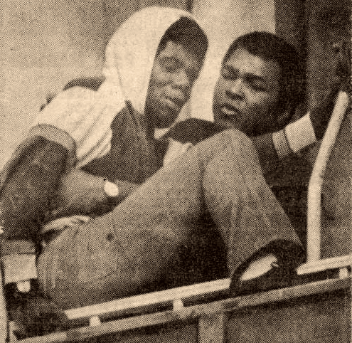 Black and white photo of Muhammad Ali holding another man while on ledge