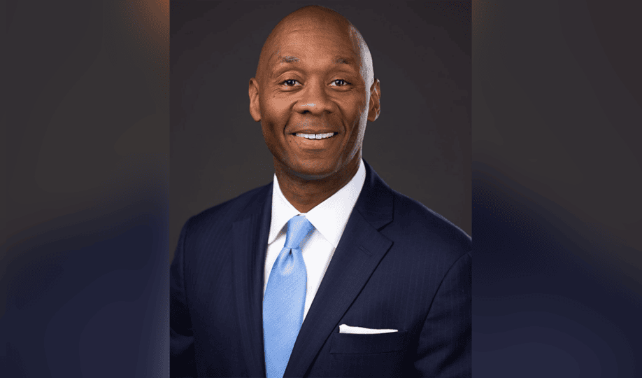 Man in black suit and blue tie smiling at camera