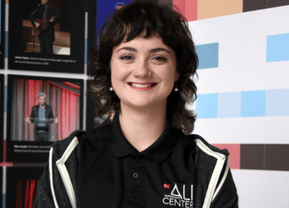 Woman with short, dark, curly hair wearing Ali Center polo and gray jacket smiling at camera