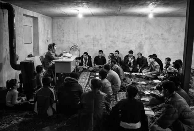 Black and white photo of woman sitting at table with group of people listening around her