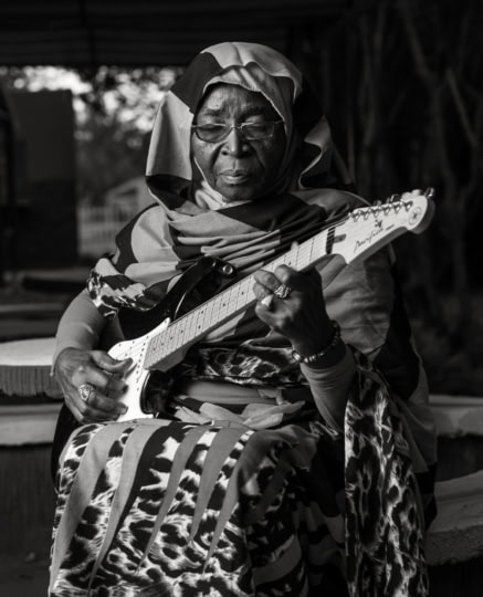 Black and white photo of woman wearing headdress and long flowing outfit strumming an electric guitar