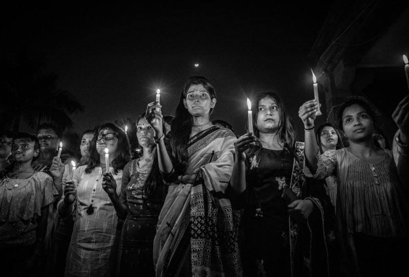 Black and white photo of women in various attire standing in group and holding up lit candles