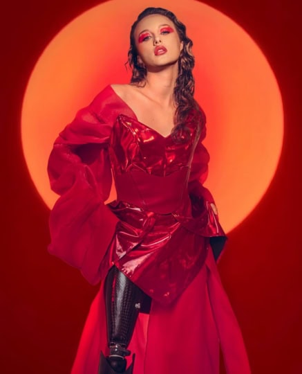 Woman with long flowing brown hair wearing red makeup and red dress showcasing prosthetic leg