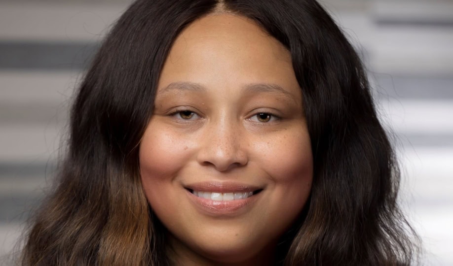 Woman with shoulder-length brown hair wearing pink sweater and necklace smiling at camera