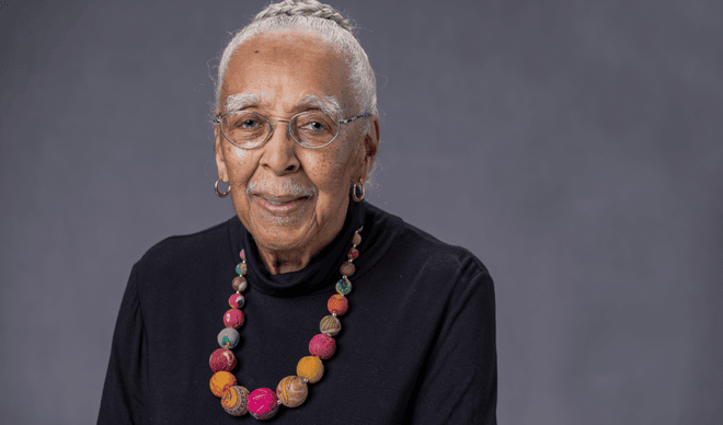 Woman with gray hair wearing black shirt and necklace looking at camera