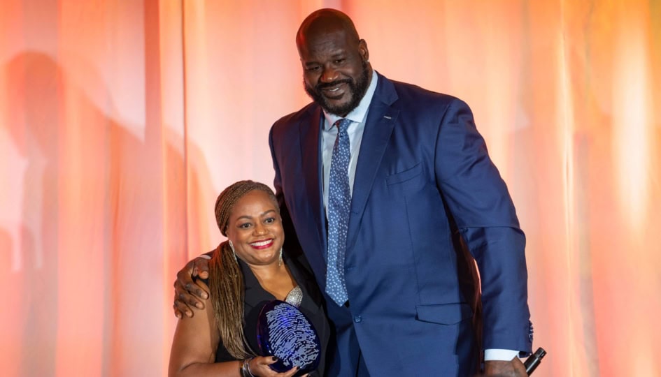 Photo of Shaquille O'Neal in blue suit posing for picture with woman in black dress holding a Humanitarian Award