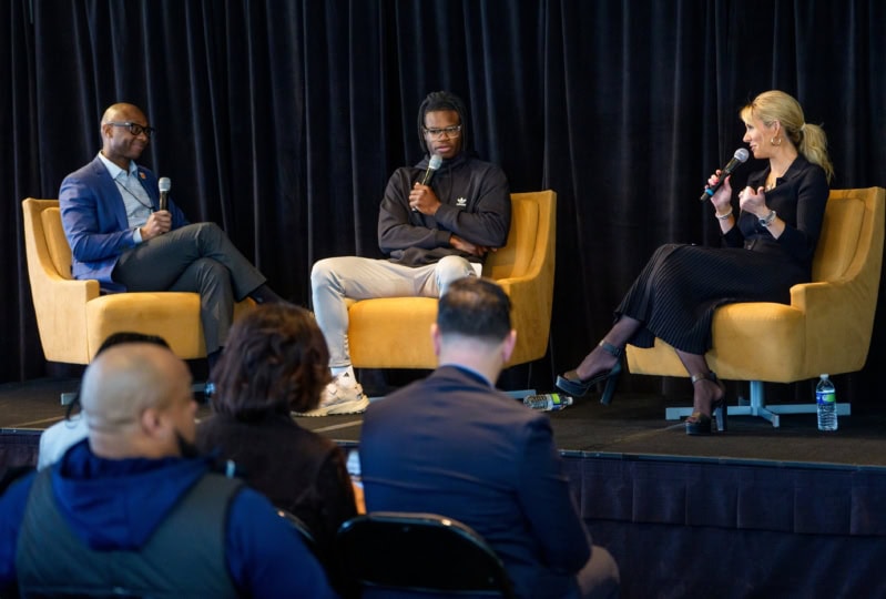 Panel discussion with three people sitting in yellow chairs holding microphones