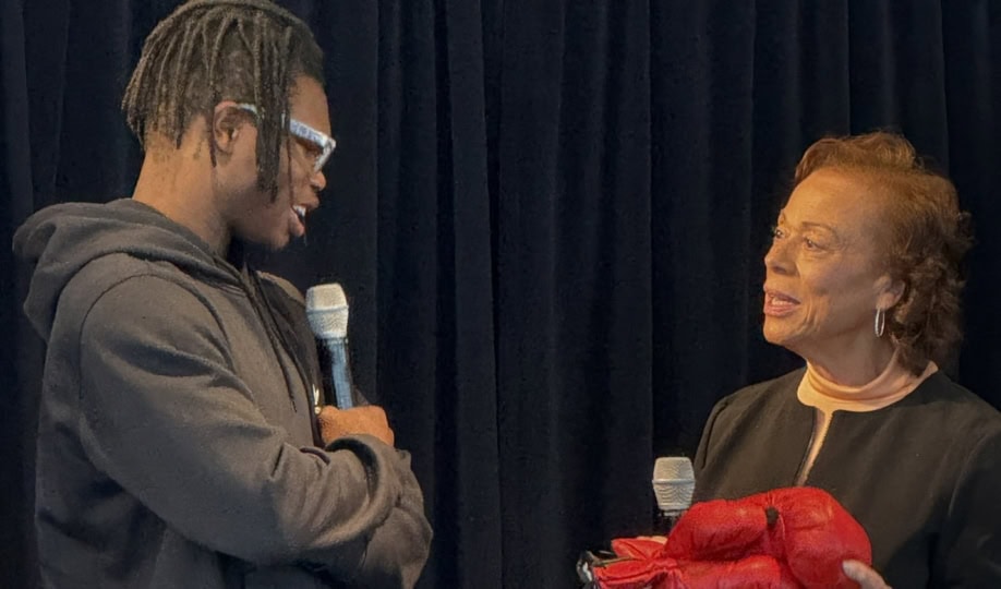 Man with microphone receives boxing gloves from woman