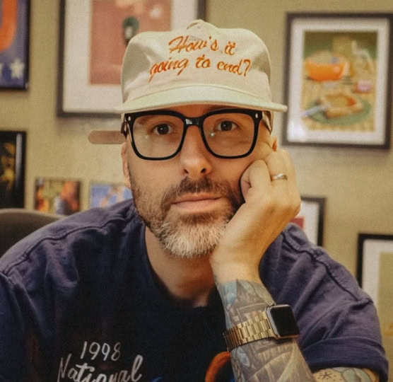 Man wearing beige hat and blue shirt with hand to face looking at camera