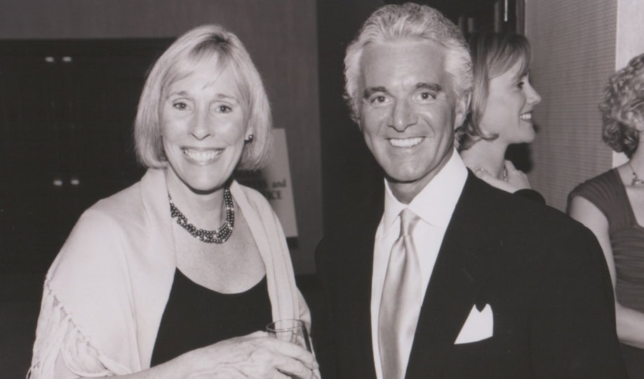 Black and white photo of woman with short blond hair wearing formal wear and man with short white hair wearing tuxedo smiling at camera