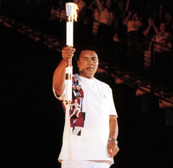 Muhammad Ali in white shirt and pants holding Olympic torch in the air