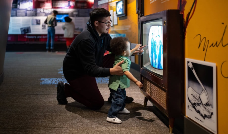 Father and young child kneeling in front of an old television in an exhibit