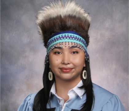 Woman wearing Native headdress and blue button up shirt looking at camera