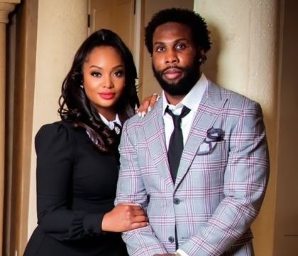 Woman with shoulder length hair and black dress standing nedxt to man in blue, purple striped suit jacket and black tie, pants smiling at camera
