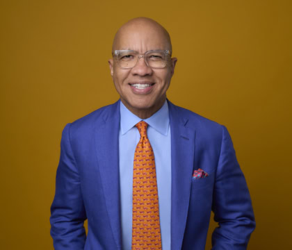 Man with glasses wearing blue suit and orange tie smiling at camera