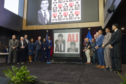 Group of people on stage in front of display showcasing the Muhammad Ali Forever stamps