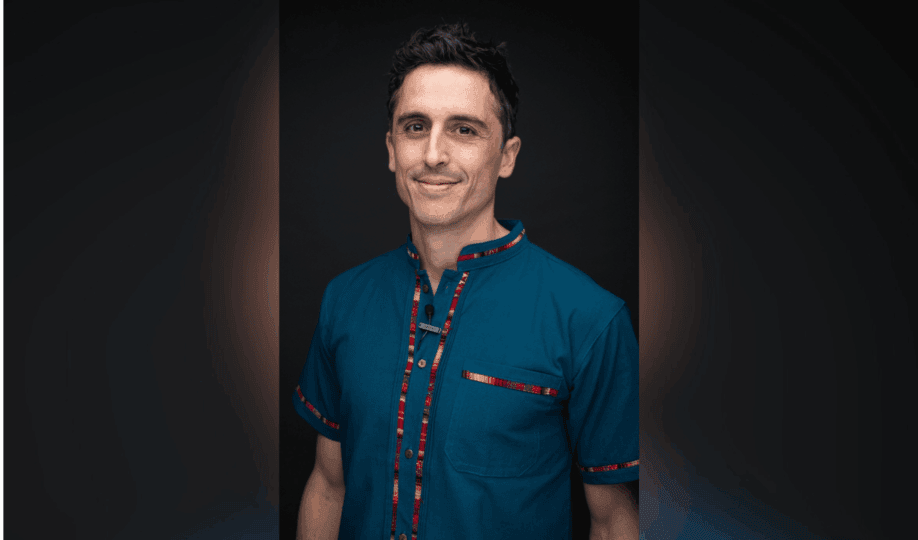 Man with short dark hair wearing blue button down shirt with multi-color edges smiling at camera