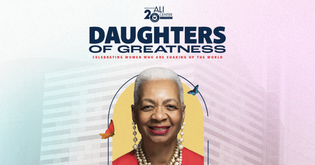 Photo of woman with short white hair wearing red top smiling placed on Ali Center backdrop with Daughters of Greatness logo