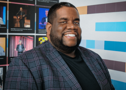 Man with dark hair wearing blue, striped blazer smiling at camera