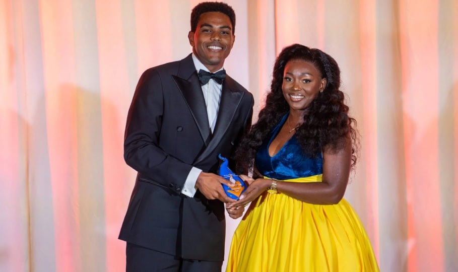 Photo of man in black suit and woman in blue and yellow dress holding award