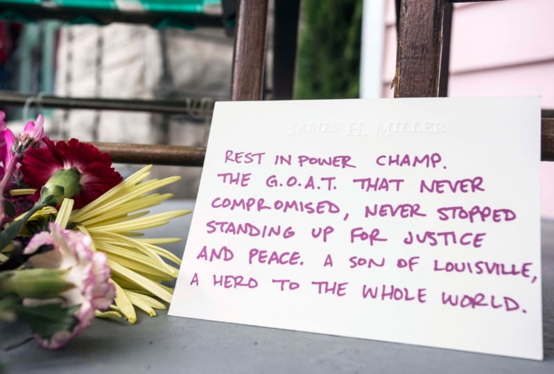 Note placed on ground with flowers that reads "Rest in power champ. The G.O.A.T. that never compromised, never stopped standing up for justice and peace. A son of Louisville, a hero to the whole world."