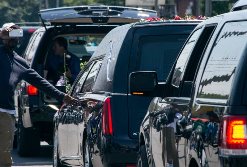 Man reaches out to touch hearse within processional line
