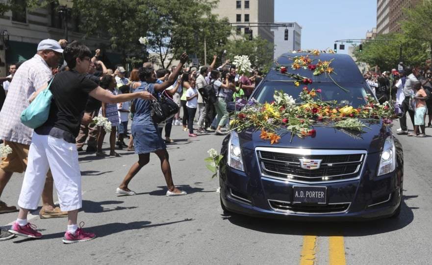 People surrounding a hearse throwing flowers onto car windshield