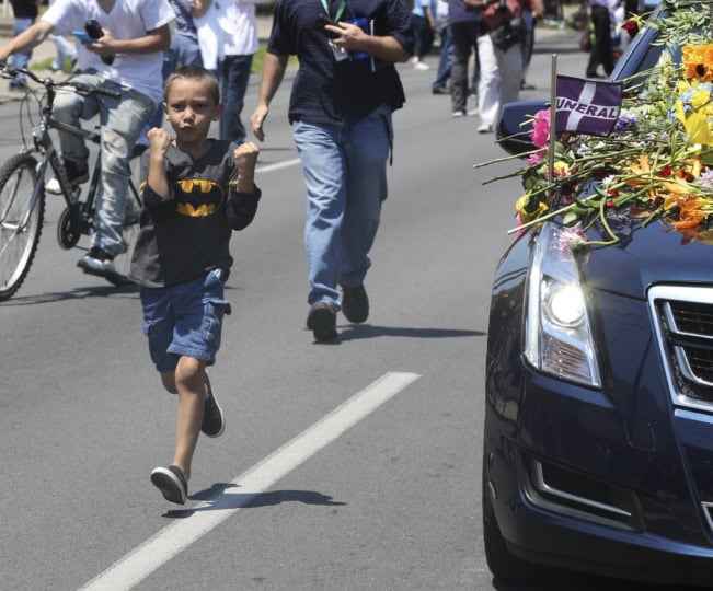Child running alongside black hearse holding up his hands in boxing pose