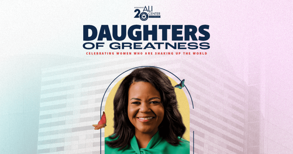 Daughters of Greatness logo with image of woman with shoulder-length dark hair wearing green shirt smiling at camera