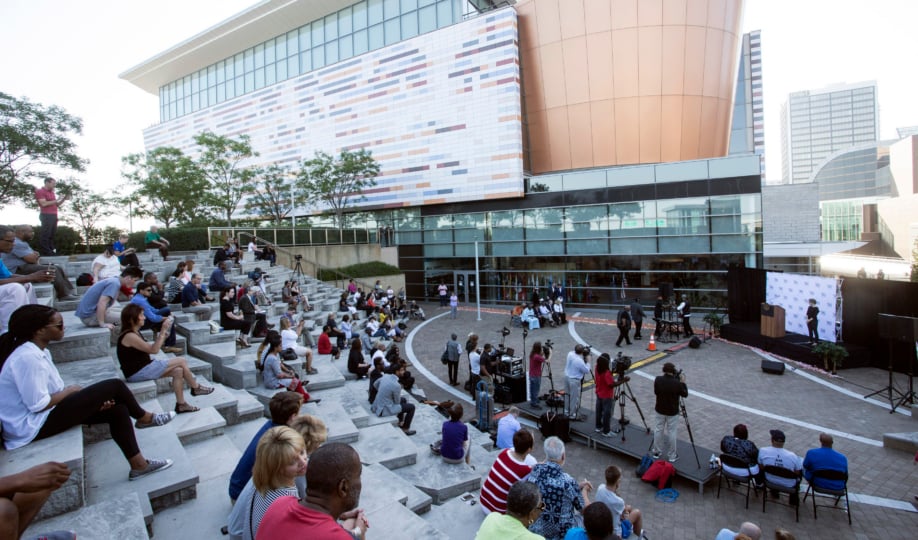 The exterior of the Muhammad Ali Center with hundreds of people gathered on stairs watching presentation on plaza
