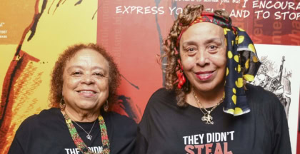 Two women wearing black shirts standing outside museum exhibit and smiling at camera