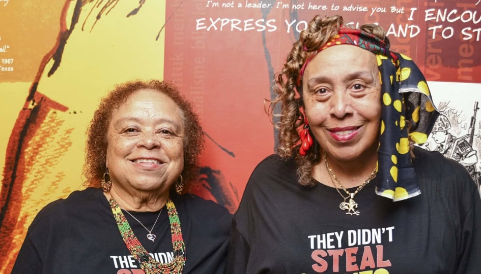 Two women wearing black shirts standing outside museum exhibit and smiling at camera