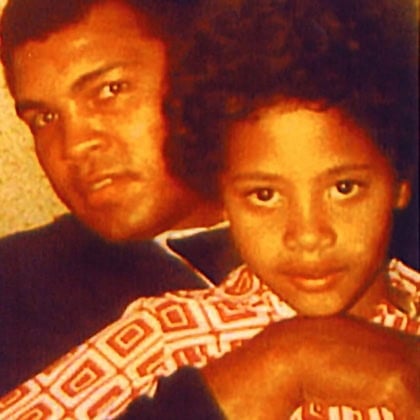 Young kid with curly hair sitting with Muhammad Ali