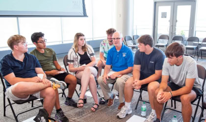 A man with a blue Hanover College polo seated with a group of students
